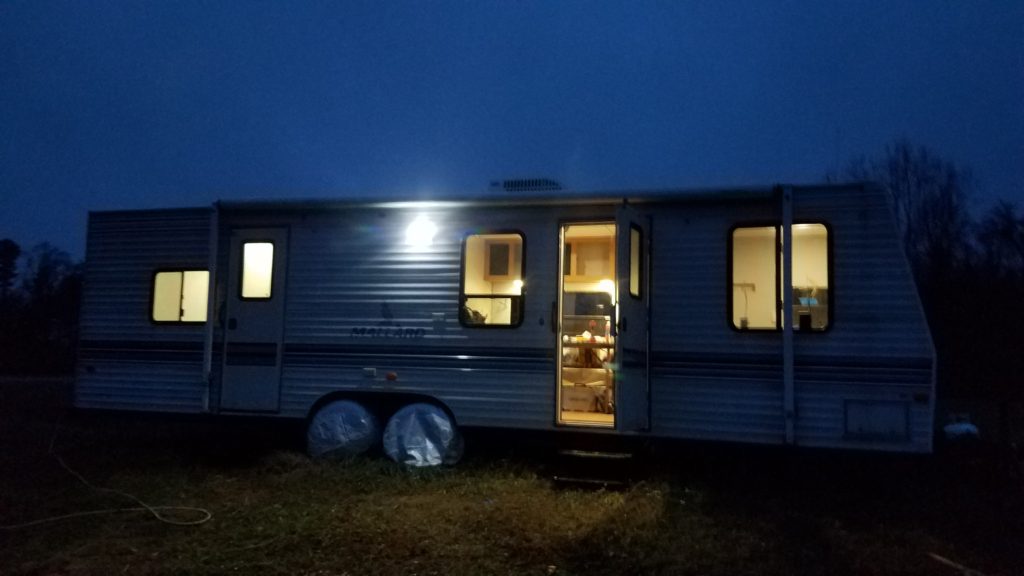 A picture of the travel trailer from outside, taken at night, with warm light shining out of the windows and the open door