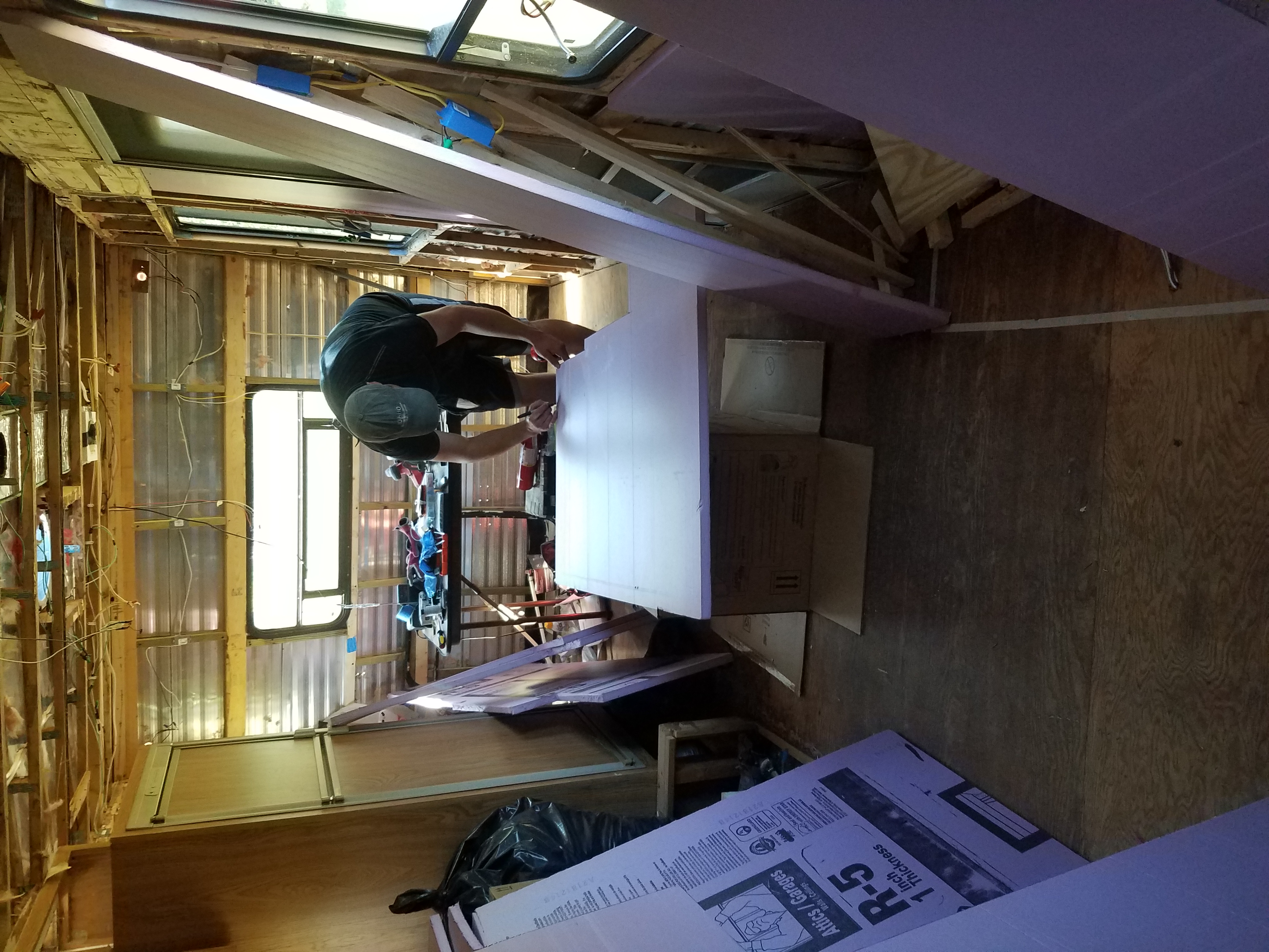 A man in a travel trailer marks foam board insulation to cut it to size