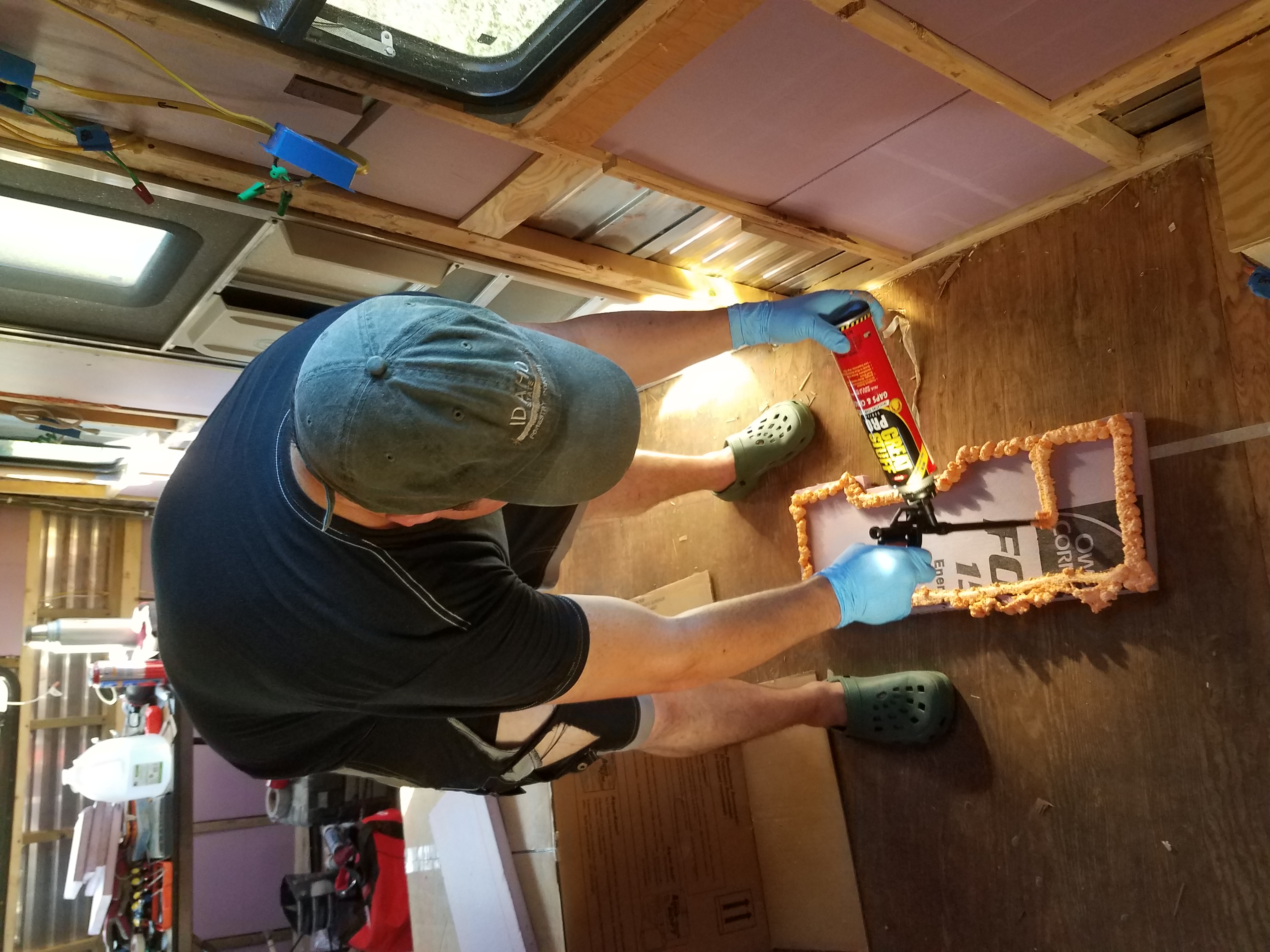 A man sprays foaming sealant on an insulation board in the travel trailer