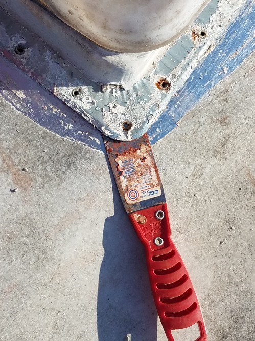 On the roof of the travel trailer, a putty knife pries up the air vent cover.