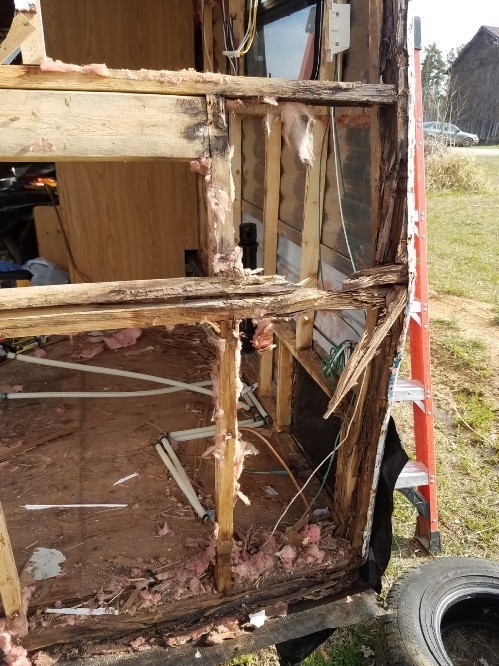 The frame of the travel trailer with the siding taken off, showing the wooden frame which is rotten and falling apart from water damage.