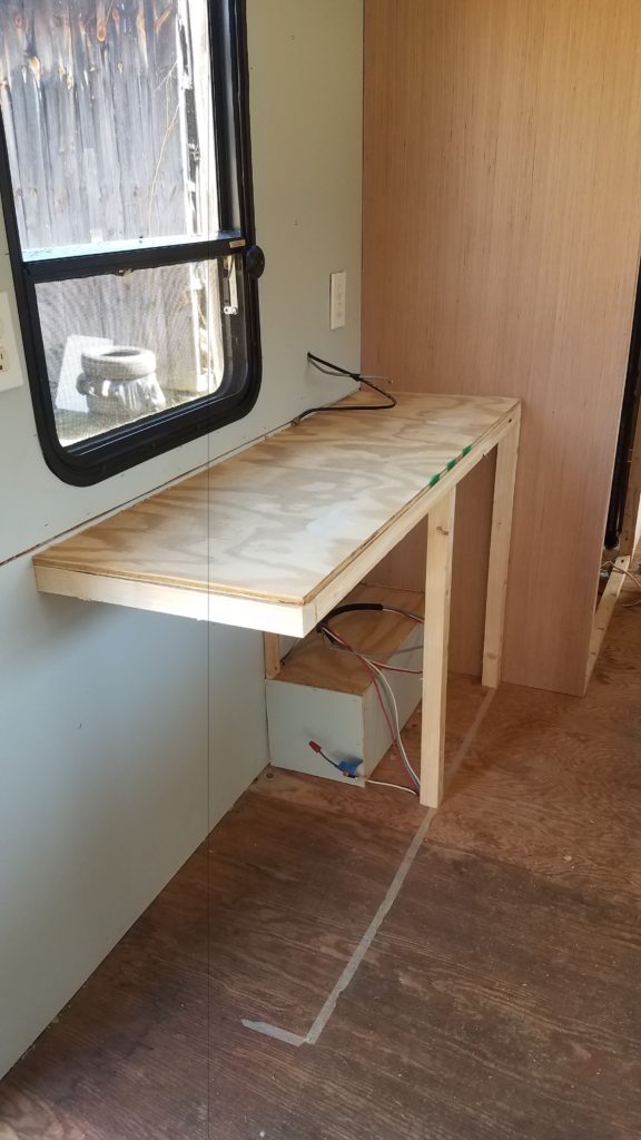A partially completed desk and cabinet under a window inside of the trailer
